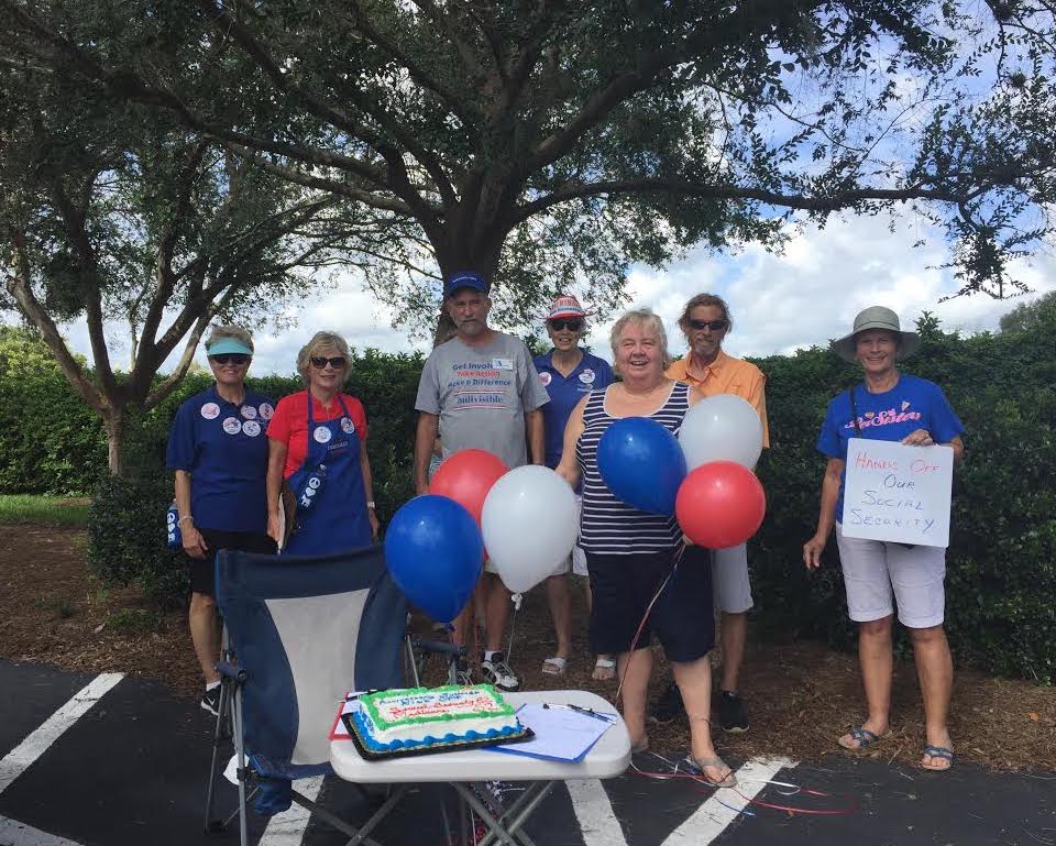 Cindy Lenhart and attendants present their cake to celebrate Medicare and Social Security's birthdays in front of Congressman Webster's Villages office.