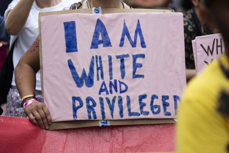 A person holding an I am white and privileged banner at a gay pride event