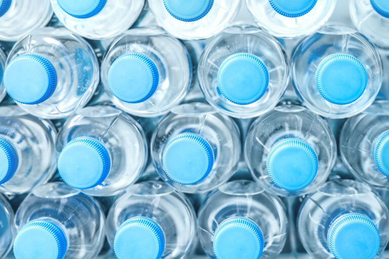 Rows of many transparent plastic bottles with drinking water supply in white refrigerator. Mineral water stack storage in fridge to drink on hot summer day. Healthcare and dehydration prevention