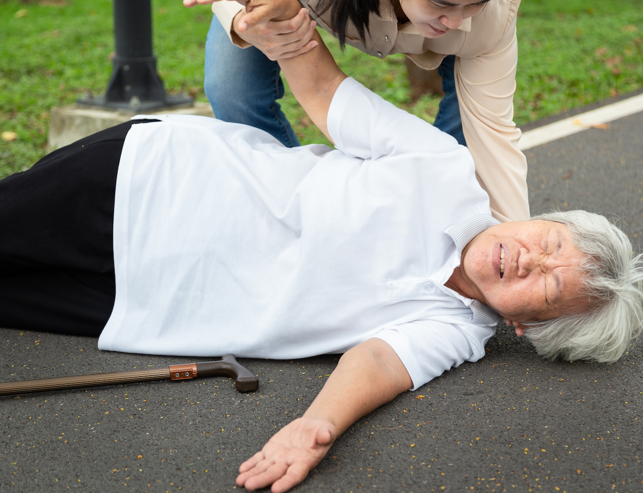 Asian elderly woman with walking stick on floor after falling down,young assistant or daughter help care to her,sick senior mother fell to the floor because of dizziness,faint,suffering from illness in outdoor park