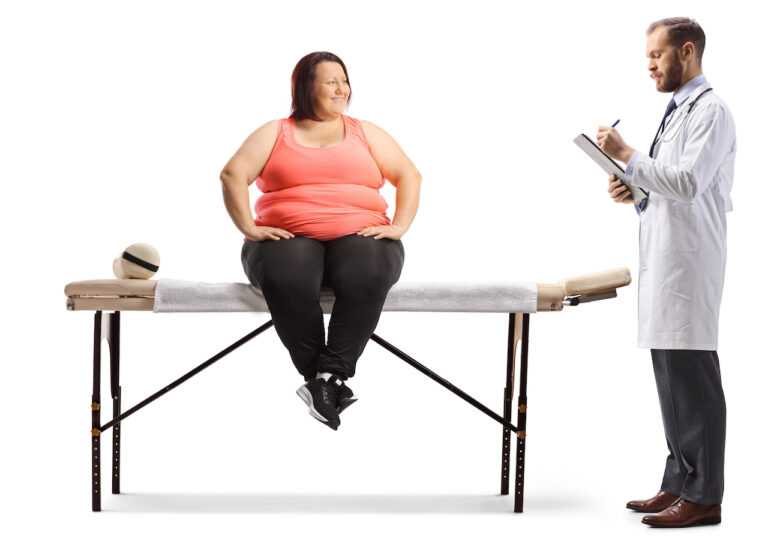 Doctor writing a prescription to an overweight woman seated on a physical therapy bed