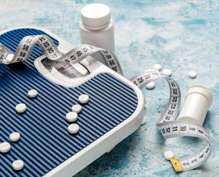 Bottles with weight loss pills, scales and measuring tape on color background
