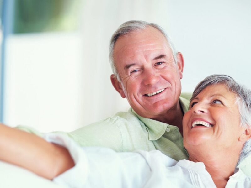 Elderly/Senior couple, happy and portrait on sofa for relax, bonding and love with support, care and together in home. Elderly people, smile and happy on couch for weekend, marriage and embrace with trust.